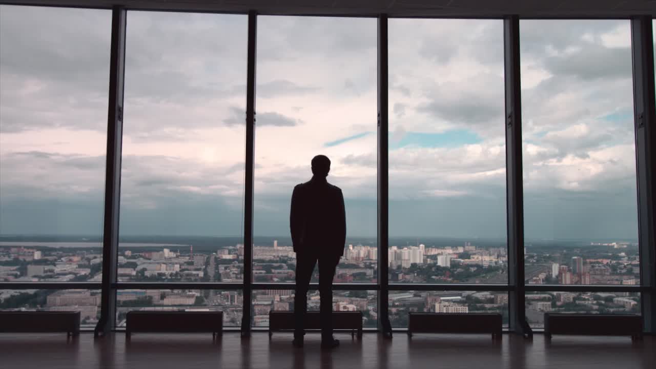 un hombre de negocios contemplando el paisaje de la ciudad desde una ventana de gran altura.