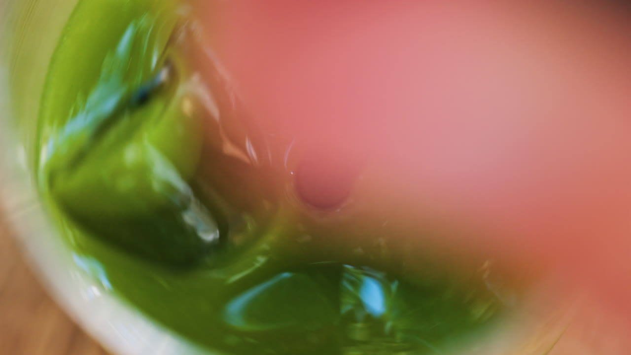 Close up of a hand mixing in a glass of an iced orange juice matcha with a black straw on a table at a cafe