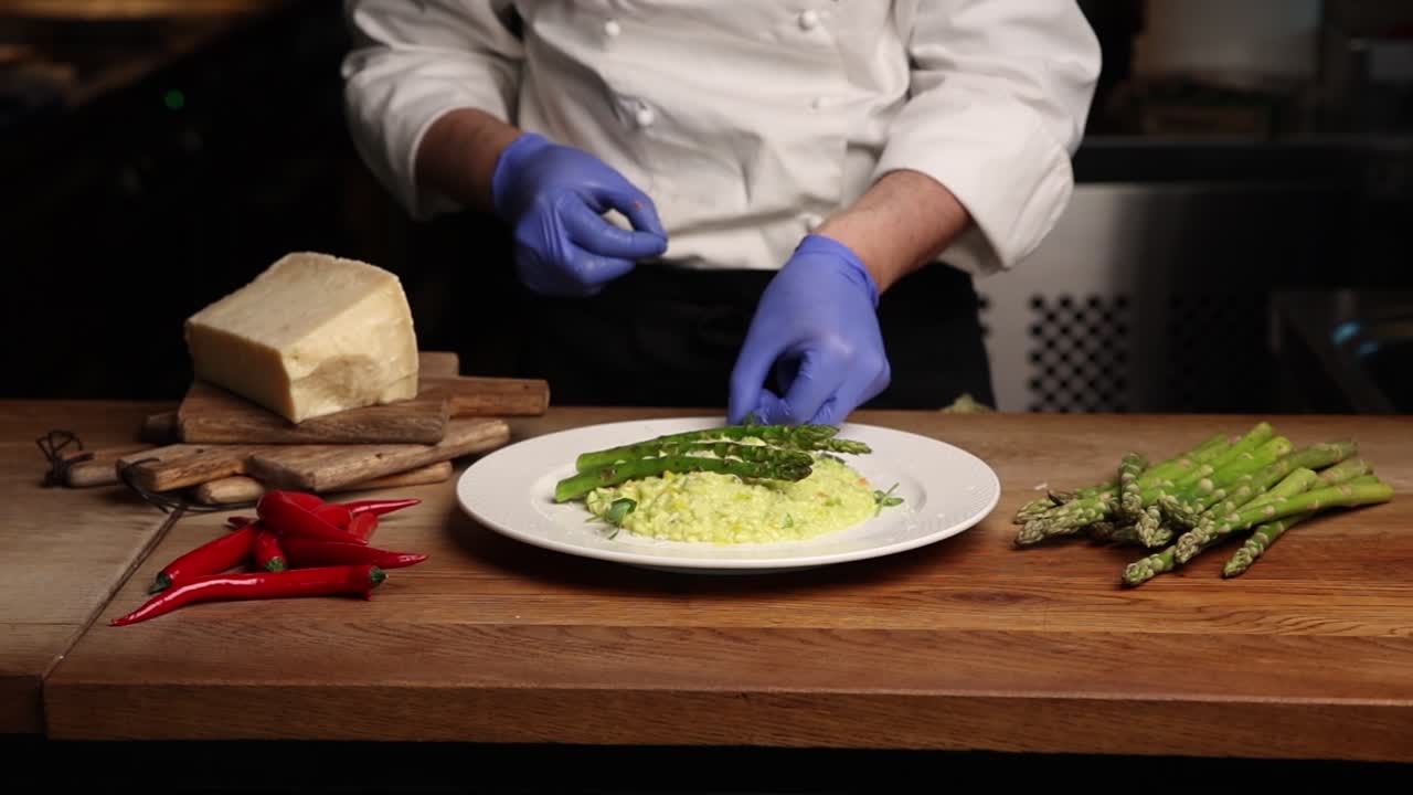 Chef che guarnisce un risotto agli asparagi in una cucina professionale