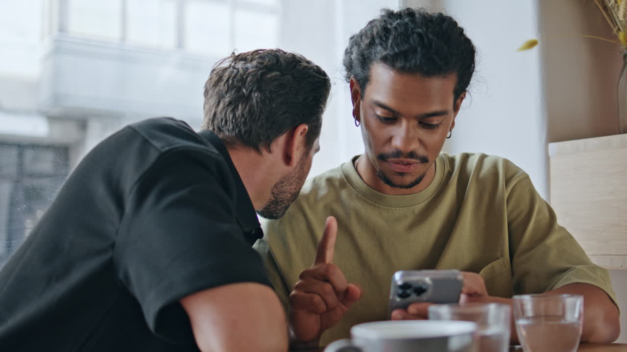 lgtb 커플이 드폰을 사용하며 커피하우스에 앉아 있다.