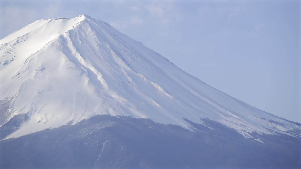 Majestic Fuji mountain close up with a pristine snow-covered summit against a clear blue sky. The landscape showcases the stunning natural scenery in this beautiful setting