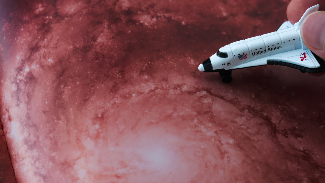 Close up of a miniature toy space shuttle placed on a reddish galaxy background
