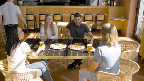 vista superior del grupo de amigos brindando con cervezas mientras se sienta en una mesa de pizzería