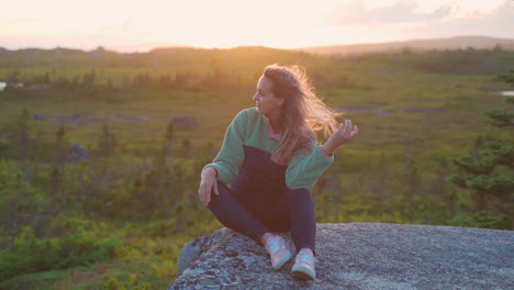 Woman-sitting-on-rocks-in-the-wilderness-in-golden-hour-sunset-smiling