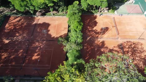 traveling-sideways-with-drone-filming-beautiful-tennis-courts-in-the-middle-of-trees-and-nature,-sunrise,-soft-light