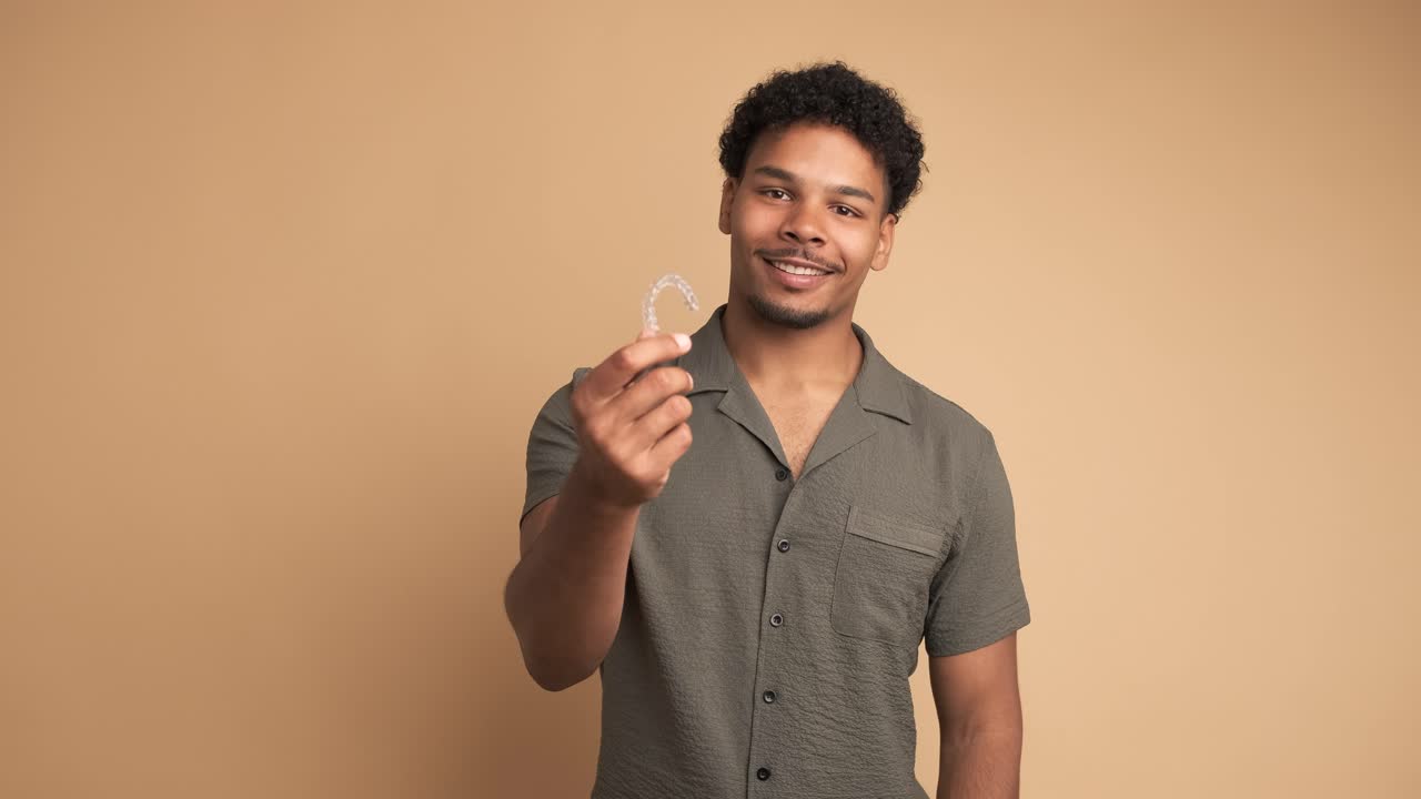 Happy young man showing invisible braces in beige studio