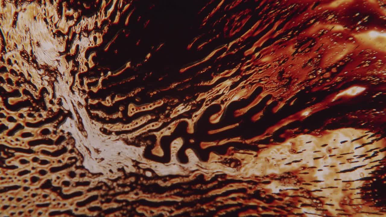 líquido negro que forma formas abstractas en una superficie naranja brillante