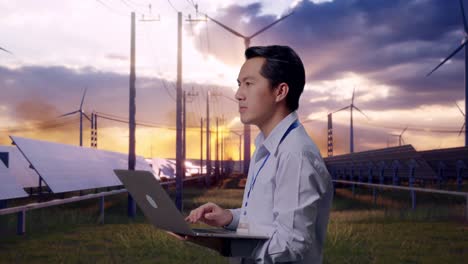 side view of an asian male professional worker standing with solar panel and wind turbines, observes by looking up before he come to concentrating on the laptop and keep on typing