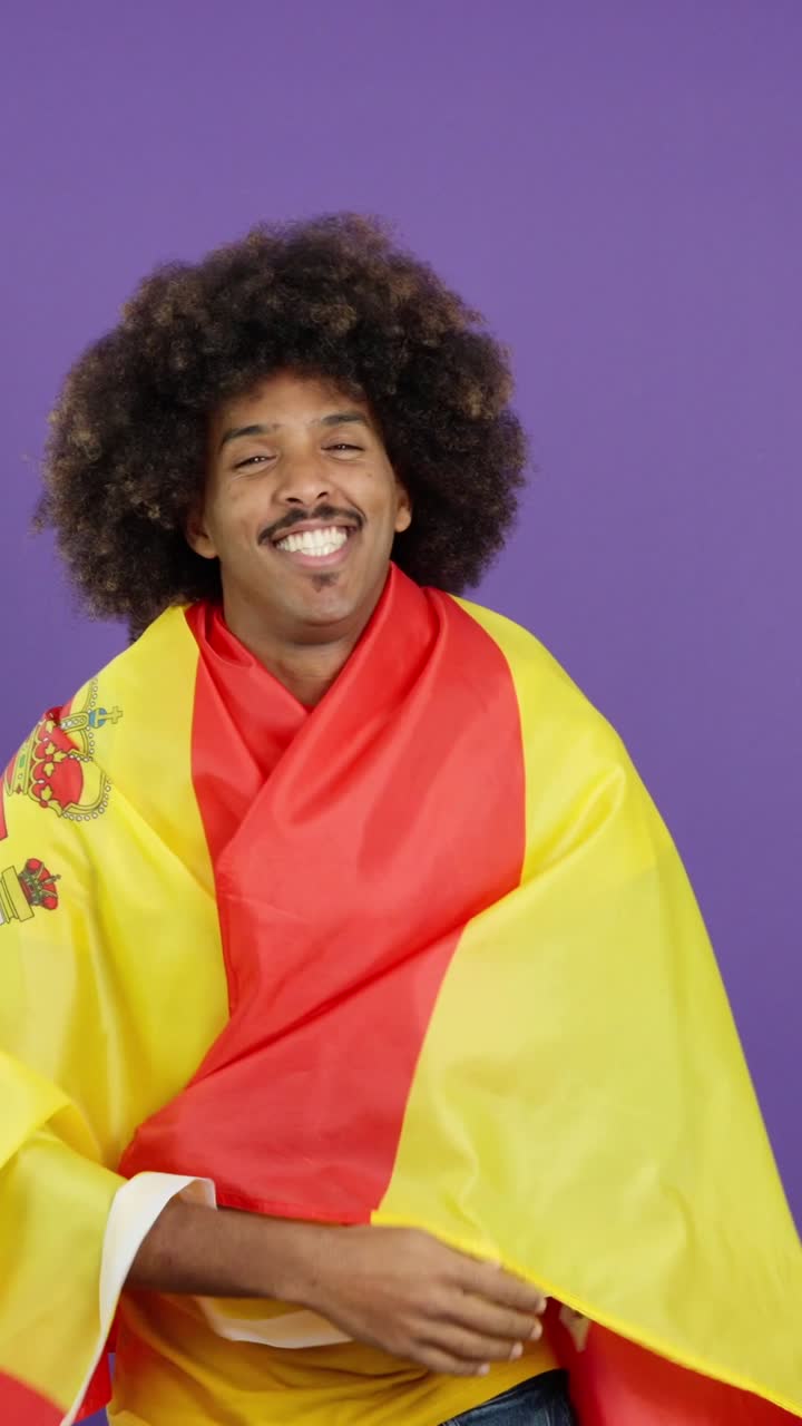 Smiling man with an afro wrapped in a Spanish flag on a purple background