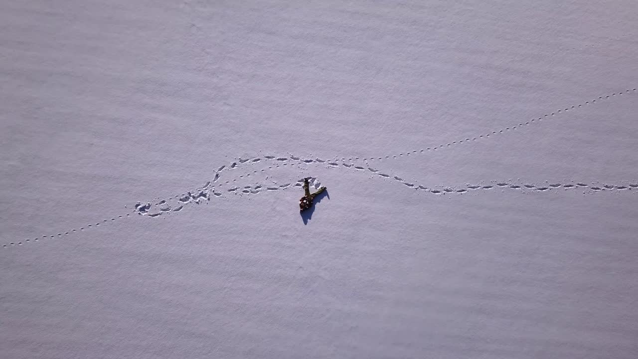 활짝 열린 눈밭에 혼자 누워 있는 스키복을 입은 청년의 드론 샷