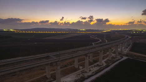 beautiful aerial hyperlapse at sunset of a massive railway bridge over agricultural fields and a road in the background