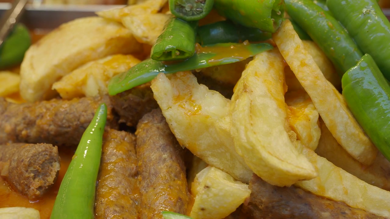 Primo piano di piatto tradizionale con salsicce, spicchi di patate e peperoncini verdi