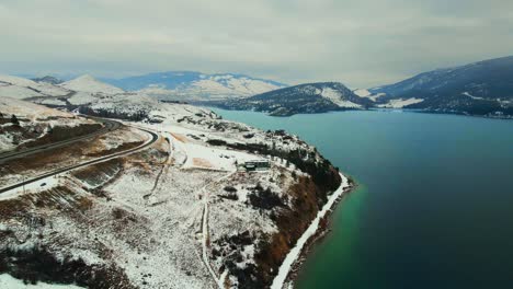 winter wonderland: turquoise wood lake in kelowna with snow-covered red cliffs and okanagan highway 97 along the shore