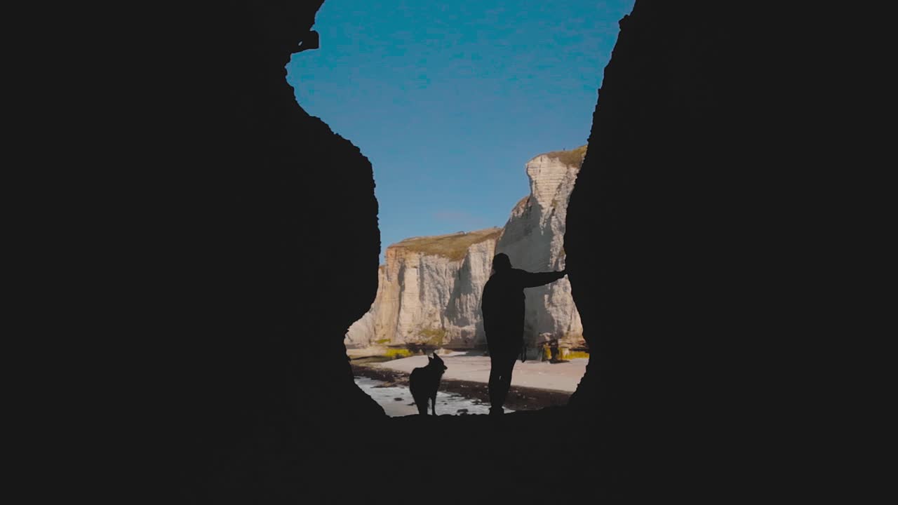 Silhouette of person and dog in sea cave with UNESCO-listed cliffs of Étretat, Normandy