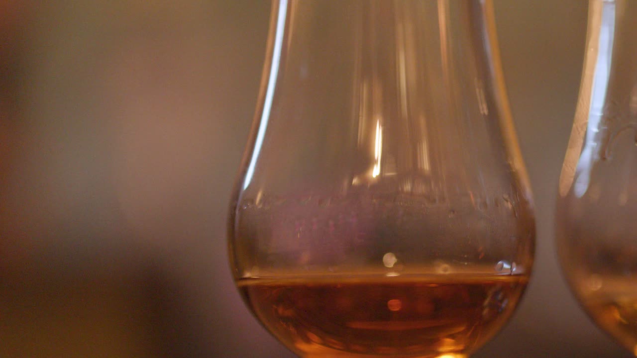 A smooth camera pan reveals several whisky glasses with amber liquid on a bar, warm ambient lighting, and a softly blurred background