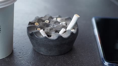 cigarette butts in ashtray and phone on a table