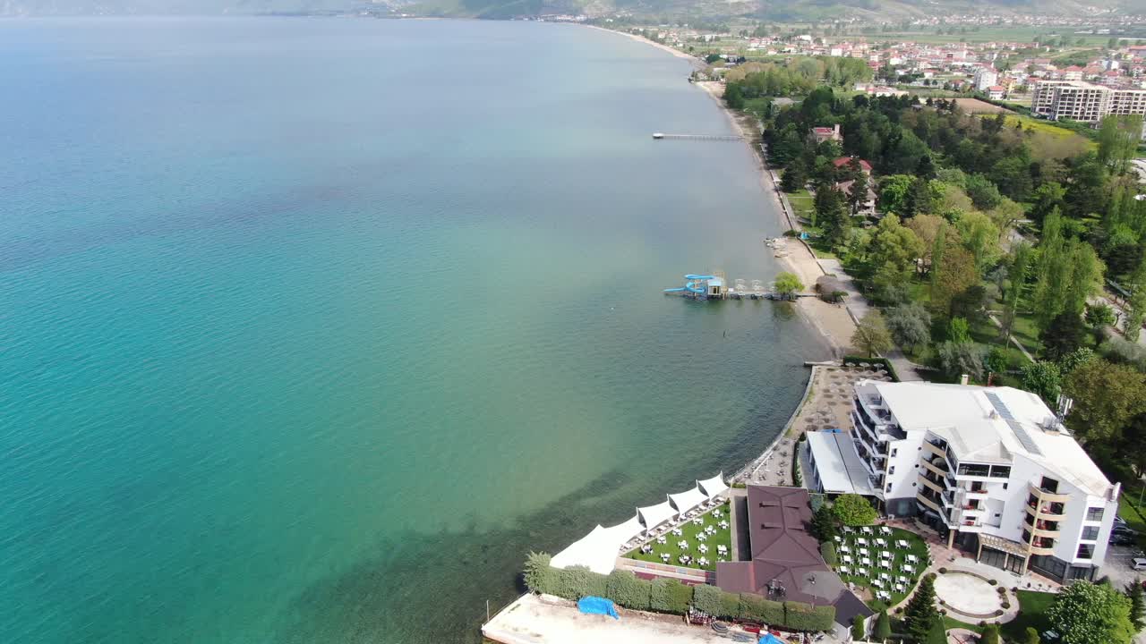 vista de drones en albania volando sobre el lago de cristal azul de ohrid en la ciudad de la playa de pogradec con edificios de apartamentos y orillas de arena
