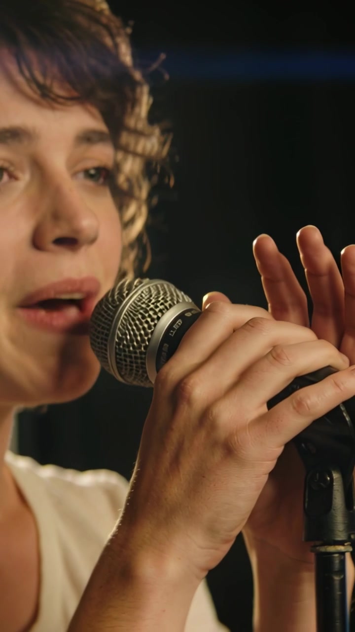 Video verticale: Faro che si accende, cantante che si china verso un microfono dinamico e canta su un palco da studio