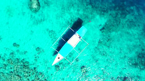 Philippine-boat-floating-on-calm-clear-water-of-azure-lagoon-over-rocky-sea-bottom,-top-down-aerial-view