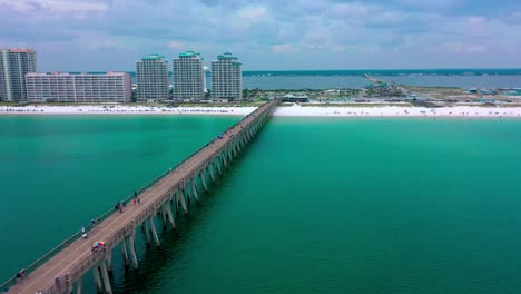 Vista-Aérea-Volando-Por-El-Muelle-De-Navarra-Beach-Fl-Mirando-La-Hermosa-Arena-Blanca,-El-Paseo-Marítimo-Y-La-Torre-De-Agua