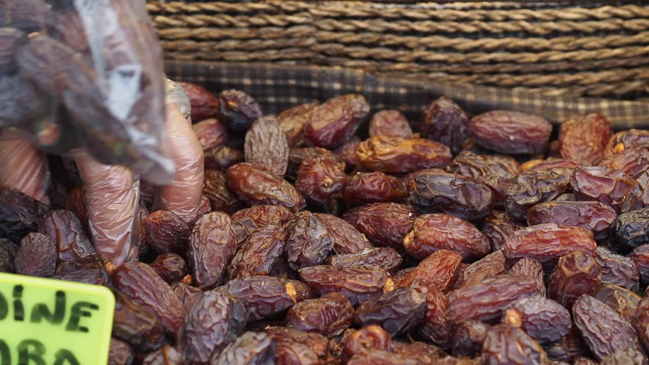 Gloved Hand Picking Fresh Dates into a Plastic Bag at a Market
