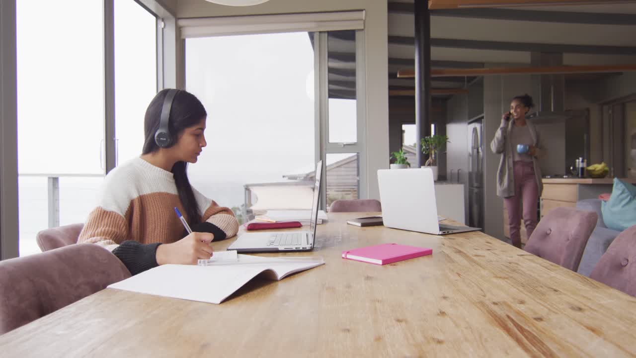 Video of focused biracial woman in headphones learning with laptop at home