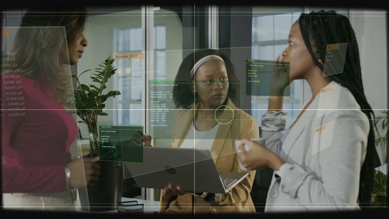 Green HUD appearing, three coworkers leaning, pointing, scrolling laptop while reviewing dashboard