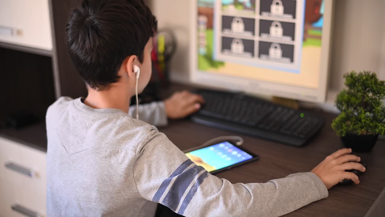 Young boy enjoys gaming at home, focused on a computer screen while also using a tablet nearby. The afternoon light fills the room, creating a cozy atmosphere