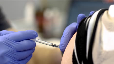 the doctor is making the injection of coronavirus vaccine to the senior female at the hospital close-up