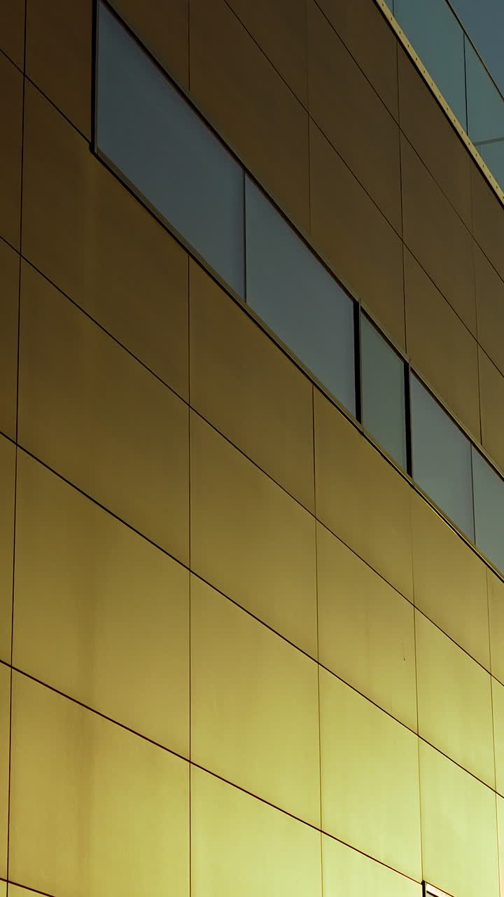 Uma imagem vertical de um edifício moderno com painéis metálicos dourados e janelas de vidro elegantes, ideal para conteúdo de imóveis e design arquitetônico.