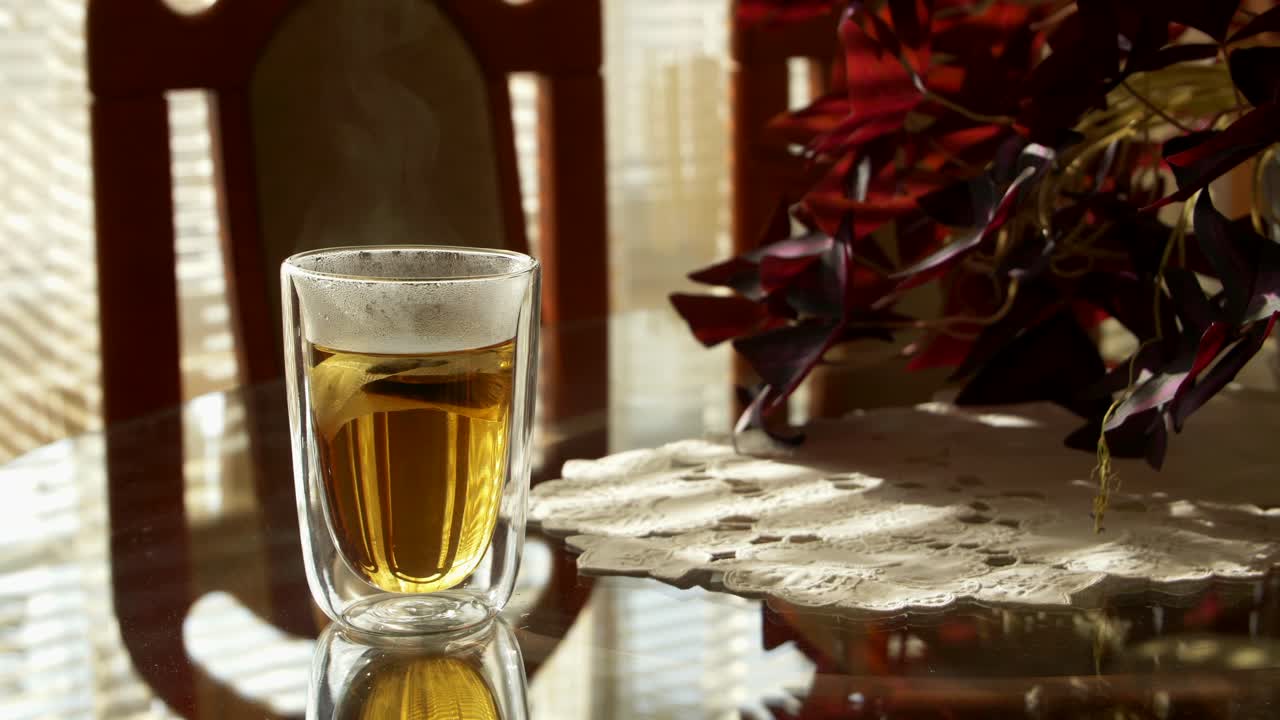 A steaming cup of tea on a table by a window