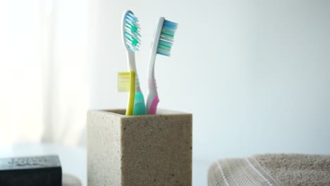 Coloridos-Cepillos-De-Dientes-En-Una-Taza-Blanca-Contra-Una-Pared