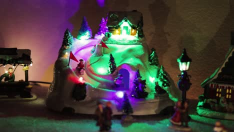 snowy miniature christmas village with a rotating ice rink and colorful lights! medium shot!