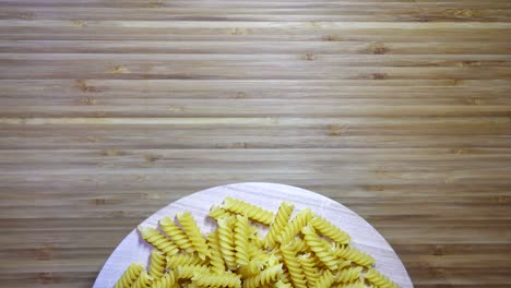04 05 - pasta de fusilli sin cocer girando sobre una tabla de cortar en blanco, en bucle