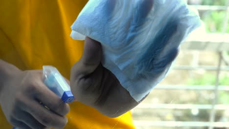 person cleaning a window with a spray bottle and tissue