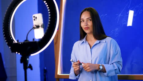 young woman on camera. in a modern studio, a young woman engages with an audience while holding a pen, appearing confident and animated