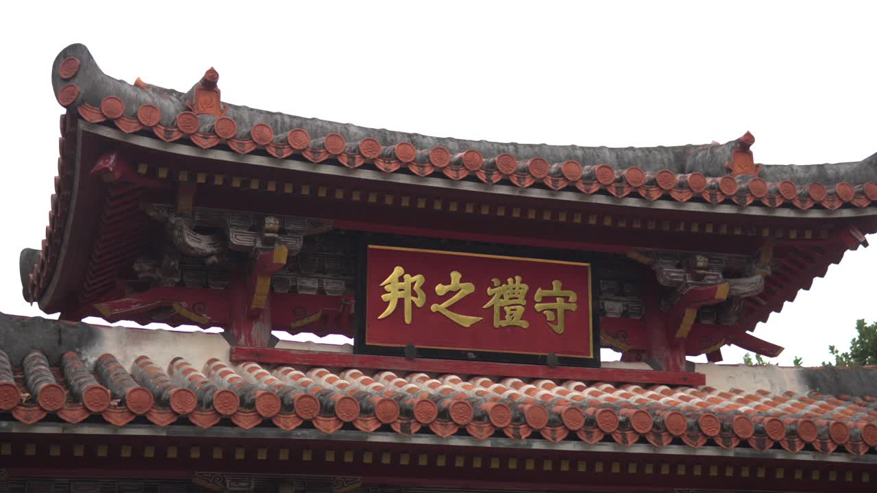 En langsom panorering afslører det ikoniske hovedskilt ved Shureimon-porten på Shuri-slottet i Naha, Okinawa, Japan. Den traditionelle røde port har fremtrædende gyldne japanske kanji-tegn