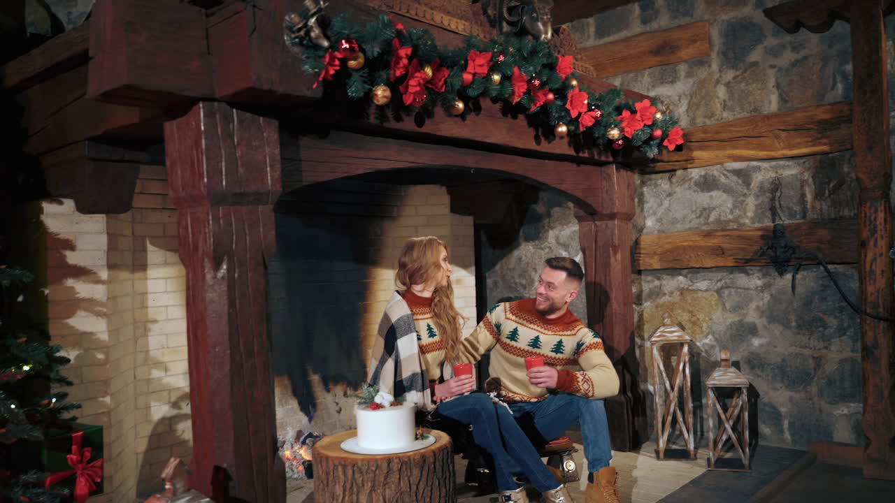 Lovely woman and man having a talk at Christmas. Young couple warming up with hot drinks by a cozy fireplace on New year background at home.