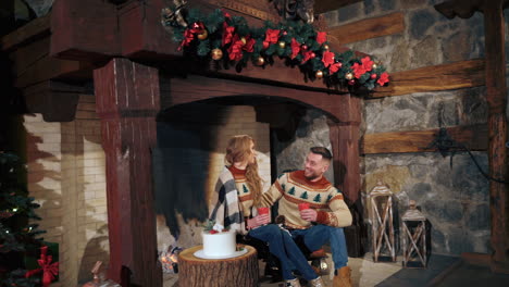 lovely woman and man having a talk at christmas. young couple warming up with hot drinks by a cozy fireplace on new year background at home.