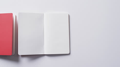 Close-up-of-closed-red-book-and-open-blank-book-with-copy-space-on-white-background-in-slow-motion