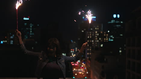 feliz joven sosteniendo bengalas bailando en la azotea por la noche celebrando la víspera de año nuevo disfrutando de la celebración navideña