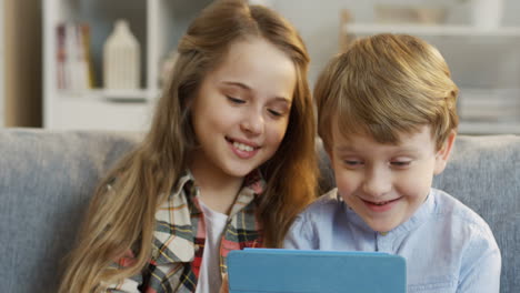 primer plano de la linda hermanita y el hermano sentados uno cerca del otro, viendo algo en el dispositivo de tableta o jugando un juego en él