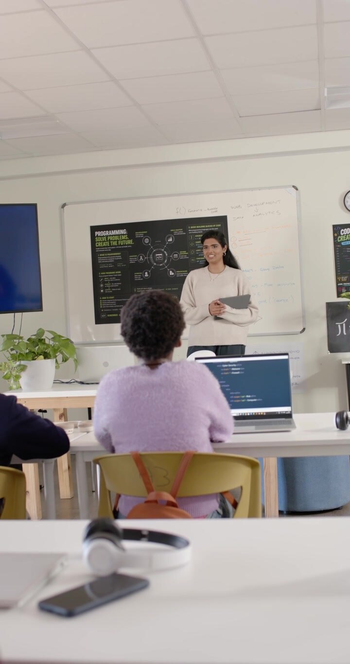 Vertical video: Woman instructor starting class in lab, gesturing, teaching coding with laptop