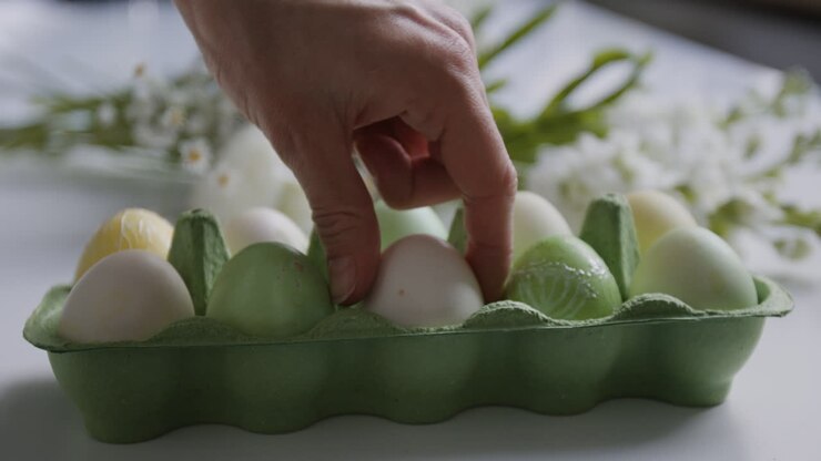 Hand arranging decorated Easter eggs in a carton