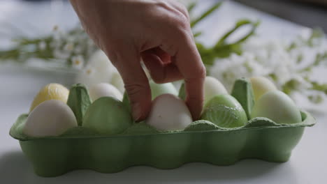 hand arranging decorated easter eggs in a carton