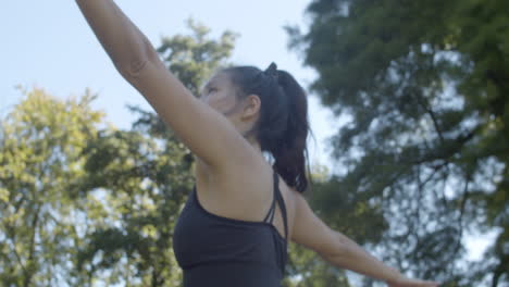 Low-angle-of-pretty-young-woman-doing-warrior-pose-in-beautiful-park