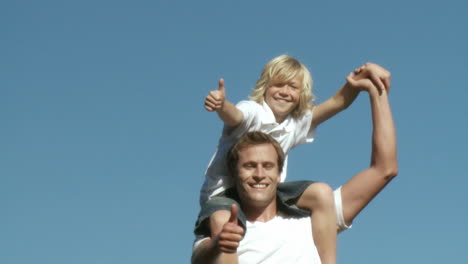 caring father with his son on his shoulders with thumbs up