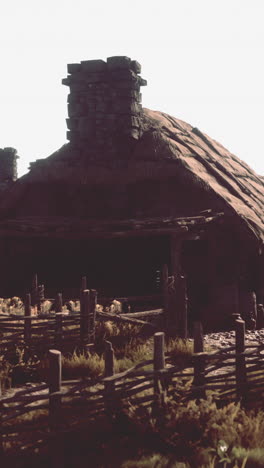 a medieval thatched-roof house with a stone chimney and a wooden fence