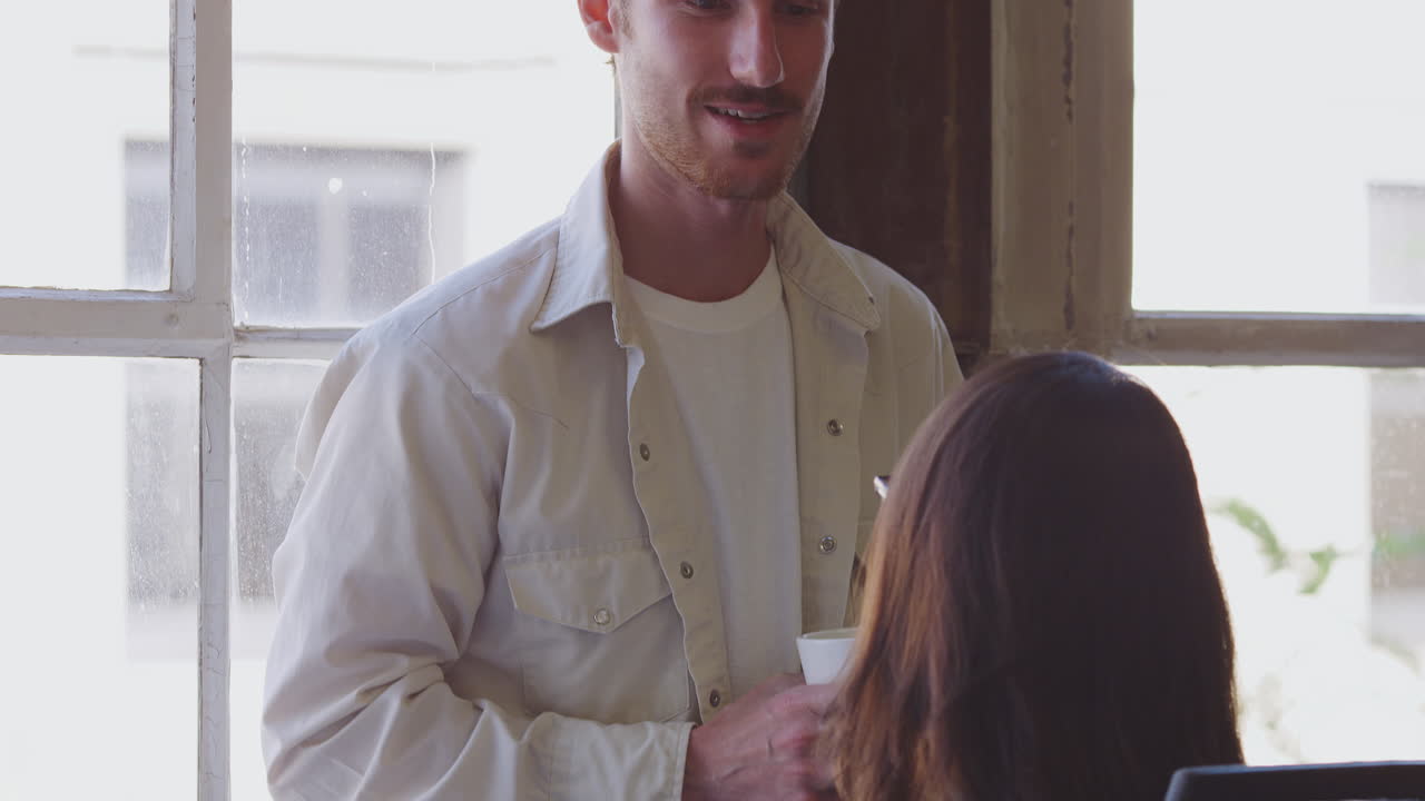 два молодых творческих коллеги делают перерыв, разговаривают в офисе, наклоняются.