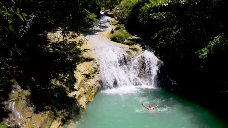 a beautiful tropical waterfall cascading into a turquoise pool, with a person enjoying a swim